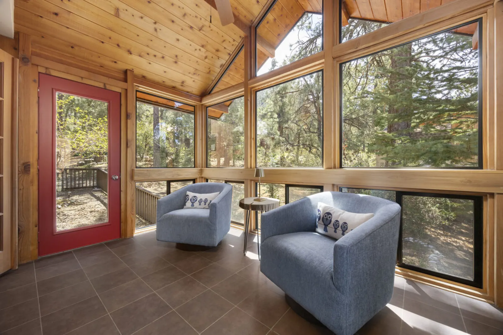 1721 Matterhorn Drive — Sunroom — cedar ceiling, walls of windows with pine forest views, and two blue lounge chairs