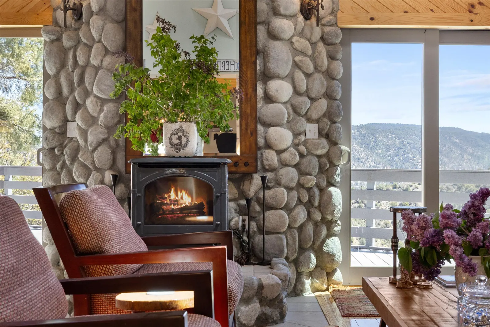 2104 St. Bernard Drive — Living room — river-rock fireplace with wood stove insert, mountain views through sliding glass doors, and wood-paneled ceiling